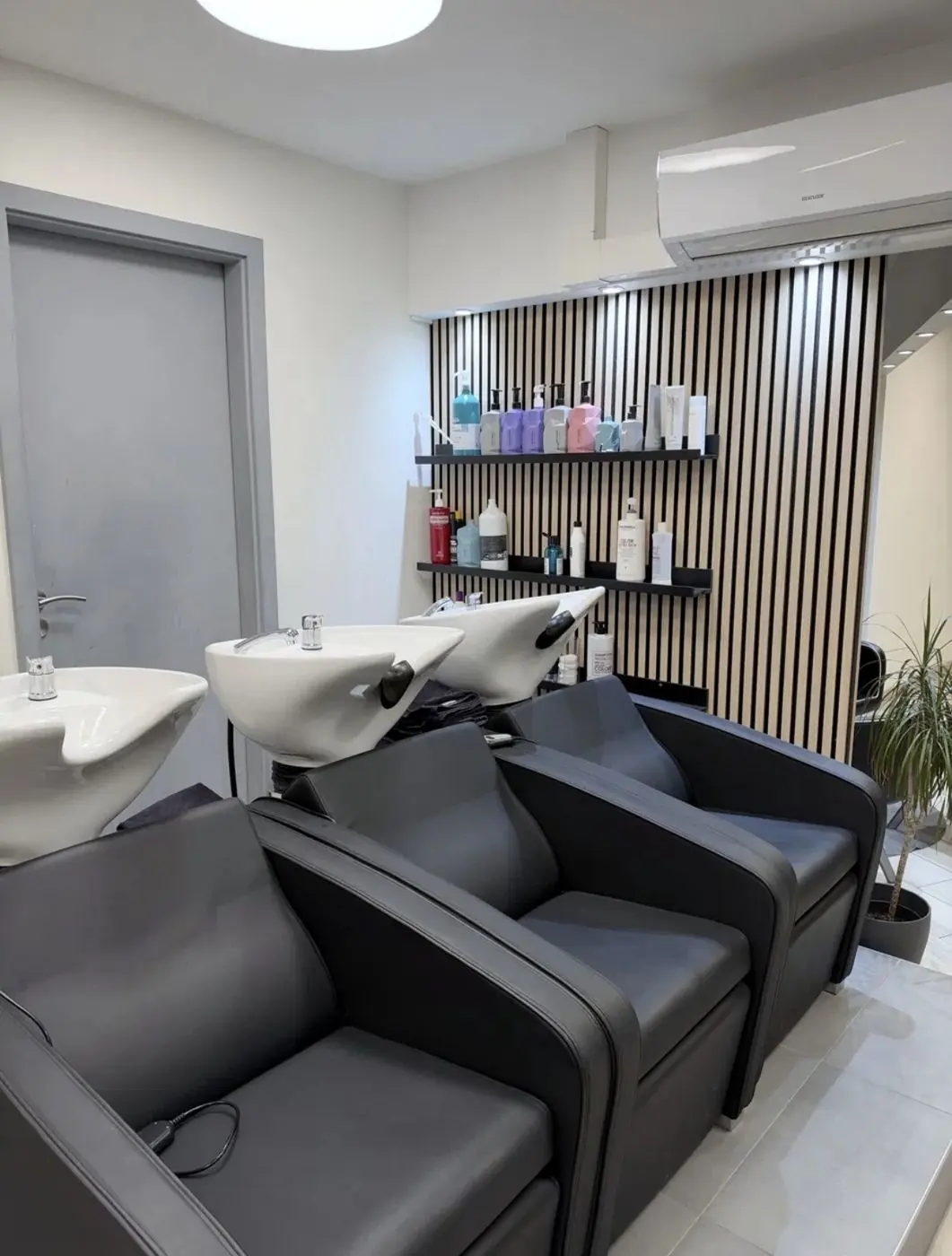 Bacs de lavage et fauteuils noirs devant le mur à lames de bois de l'espace coiffure